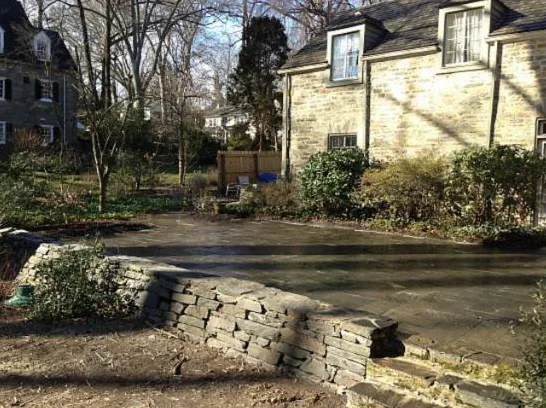Natural stone wall along a bluestone patio in front of a stone home
