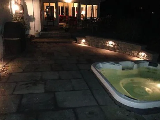 Flagstone patio around a hot tub with low stone wall lighting at dusk